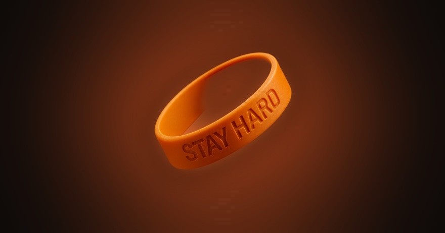 The orange STAY HARD silicone band, glowing on an ember background
